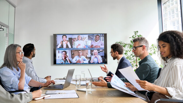 Diverse employees on online conference video call on tv screen in meeting room.